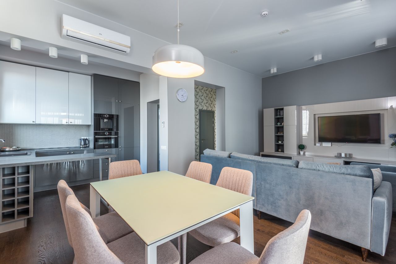 about-img Spacious open-plan living area with modern furnishings, featuring a dining table, sofa, and kitchen.